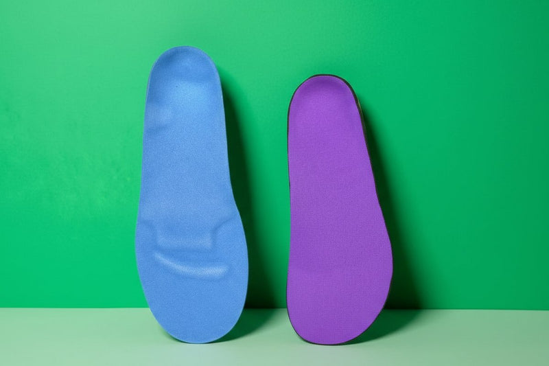 two CustomTread orthotic insoles in blue and purple leaning against a green background, product photography