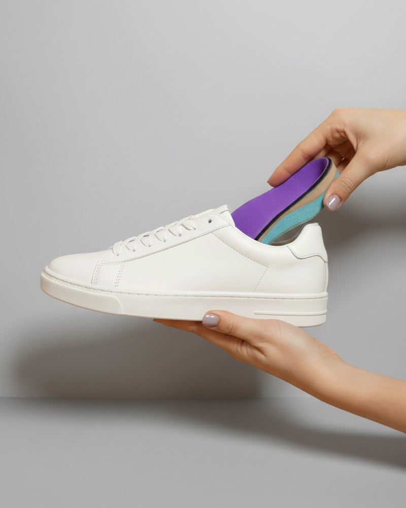 White sneaker with a purple and blue insole held by a hand against a gray background
